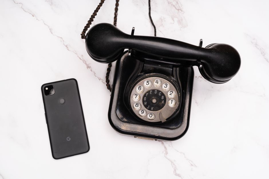 A top-down view of a vintage rotary phone and a modern smartphone placed on a marble surface, showcasing technology evolution.